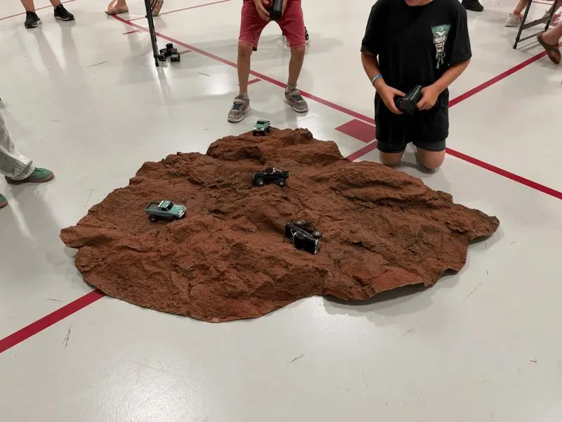 A boy holding a controller over a rock terrain mat with several small trucks